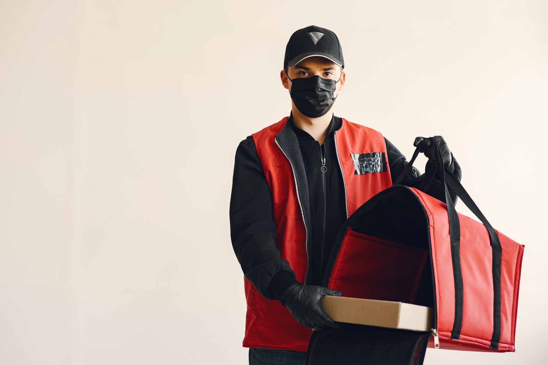 Young pizza delivery man in uniform and protective mask